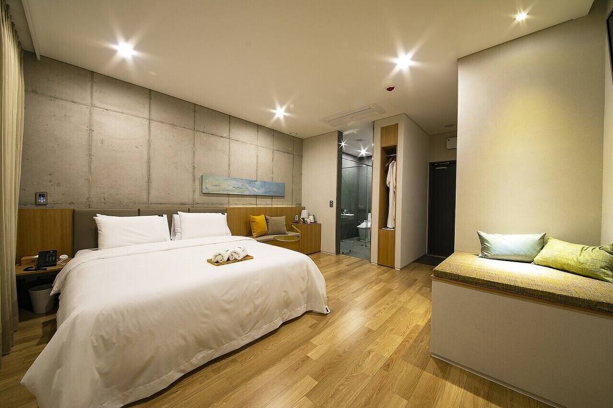 A modern hotel room with a large bed, bedside tables, a seating area, and a view of the bathroom.