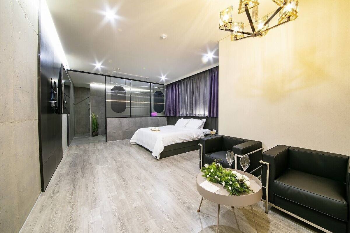 A modern hotel room with a bed, a sofa, a small table with a vase, and a TV.