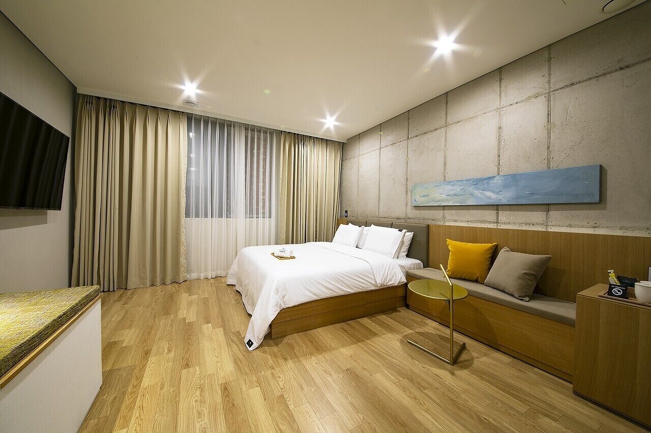 A modern hotel room with a wooden bed, a sofa, a small table, and a painting on the wall.