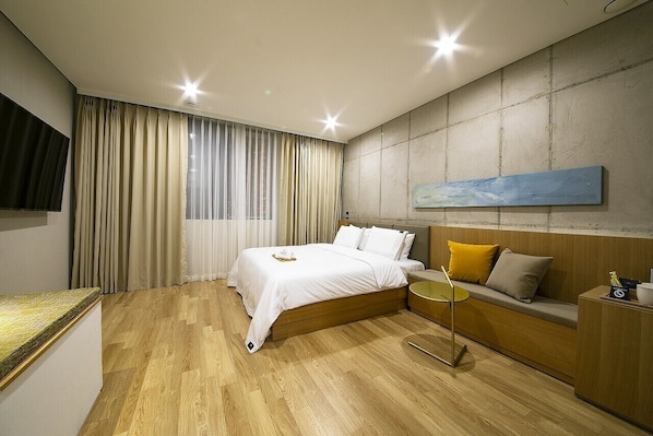 Habitación de hotel moderna con una cama de madera, un sofá, una mesita y un cuadro en la pared.