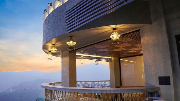 Un balcón con vistas a una cadena montañosa, una barandilla y luces colgantes.