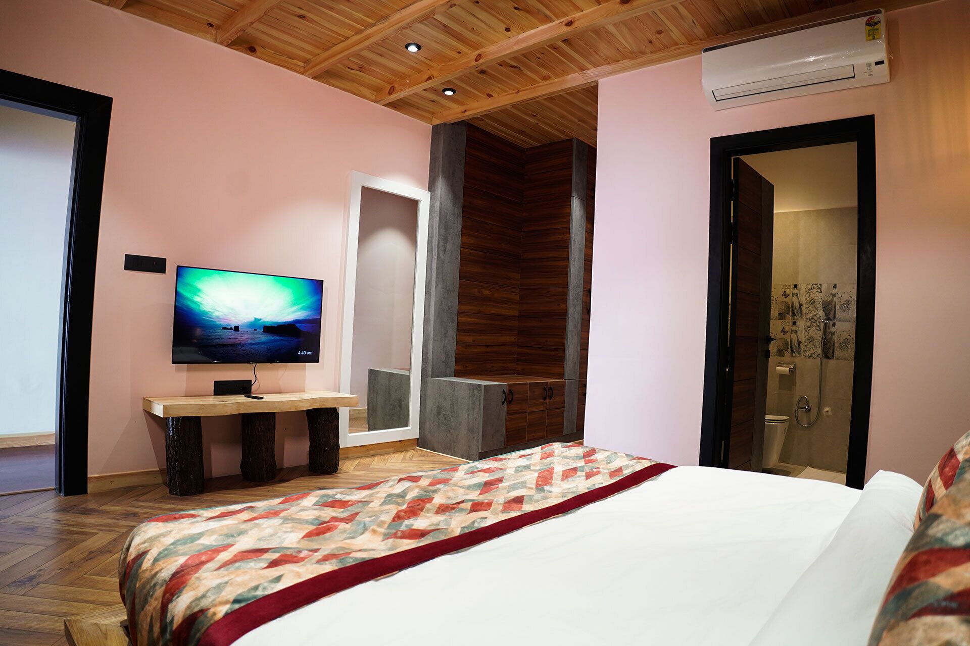 A bedroom with a bed, a TV, a wooden ceiling, and a shower area.