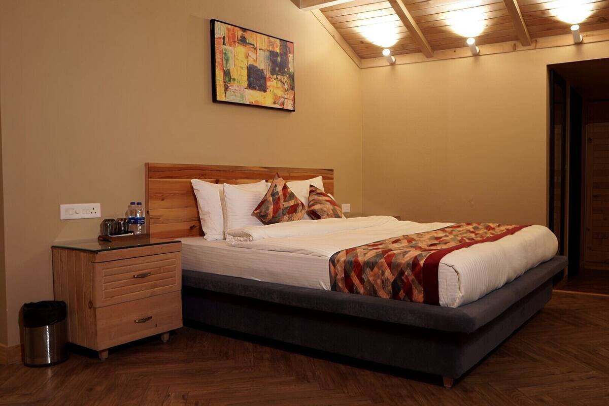 Ein Schlafzimmer mit einem hölzernen Kopfteil, einem Bett mit weißer Bettwäsche, einer gemusterten Tagesdecke, einem Nachttisch mit Lampe und einer Mülleimer.