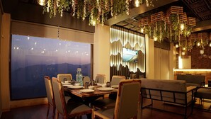 Comedor con un amplio ventanal, sillas y mesa de madera dispuesta para una comida, y plantas colgantes.