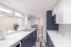 A modern kitchen with a marble countertop, dark cabinetry, and a view through an open door.