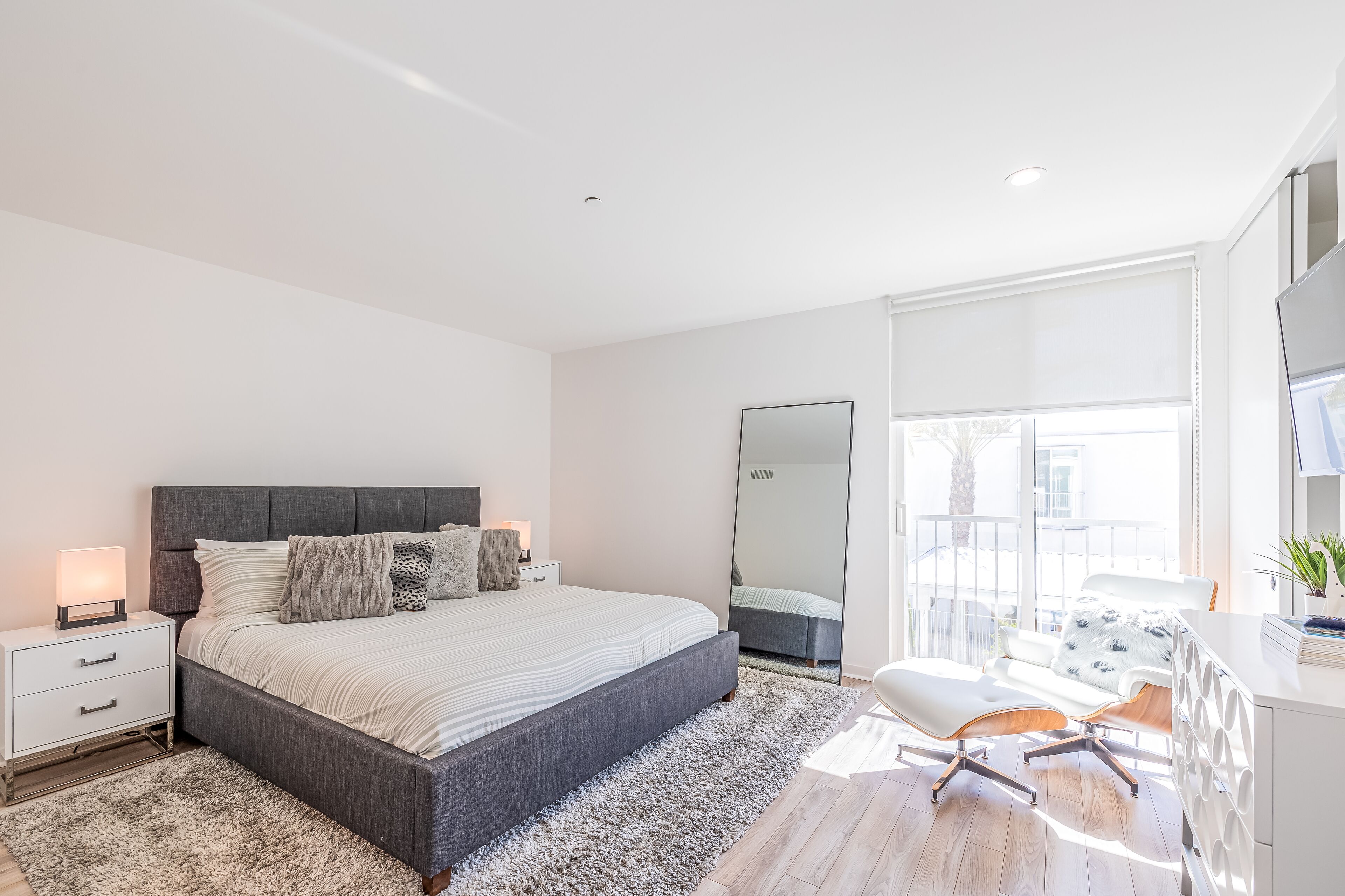 A modern bedroom with a large bed, bedside tables, a desk, and a large mirror.