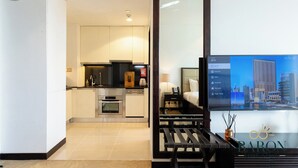 A modern hotel room with a kitchen area, a bed with a headboard, and a large window with a cityscape view. - Stunning Studio JW Marriott Marina (Dubai)