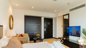 A hotel room with a large bed, a sofa, a small table with a vase, a TV, and a door leading to another room. - Stunning Studio JW Marriott Marina (Dubai)