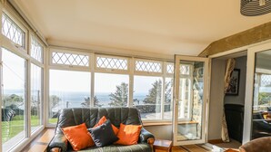 A room with a leather sofa, wooden side table, and a view of the outdoors through large windows. - Mynydd ar Mor (Barmouth)