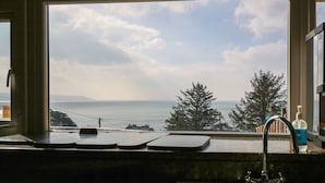 A kitchen with a large window overlooking a scenic view of trees and the ocean. - Mynydd ar Mor (Barmouth)