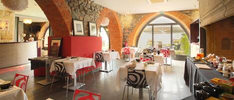Un restaurante con arcos de ladrillo, mesas blancas y vistas al exterior con vegetación.