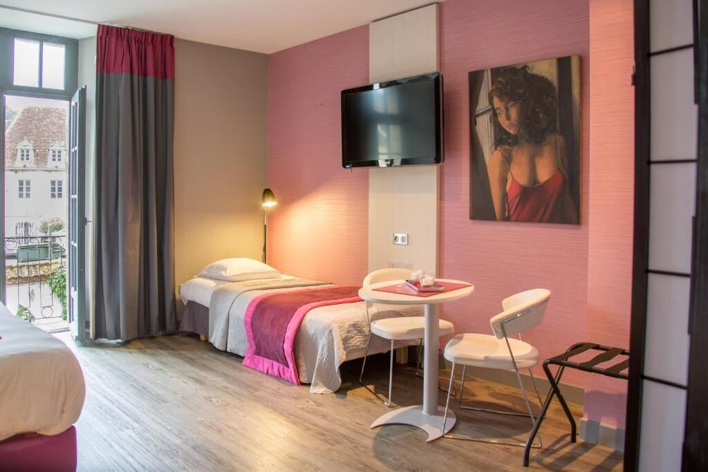 Une chambre d’hôtel avec un lit, un bureau avec des chaises, un téléviseur fixé au mur et un tableau.