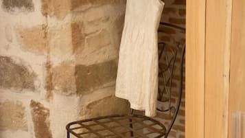A room with a stone wall, a metal chair, a wooden cabinet, and a white dress hanging on a rack.
