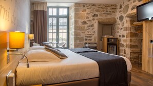 A modern hotel room with a stone wall, a large bed with white and dark bedding, a flat-screen TV, and a wooden nightstand. - Hôtel Le Turenne (Beaulieu-sur-Dordogne)