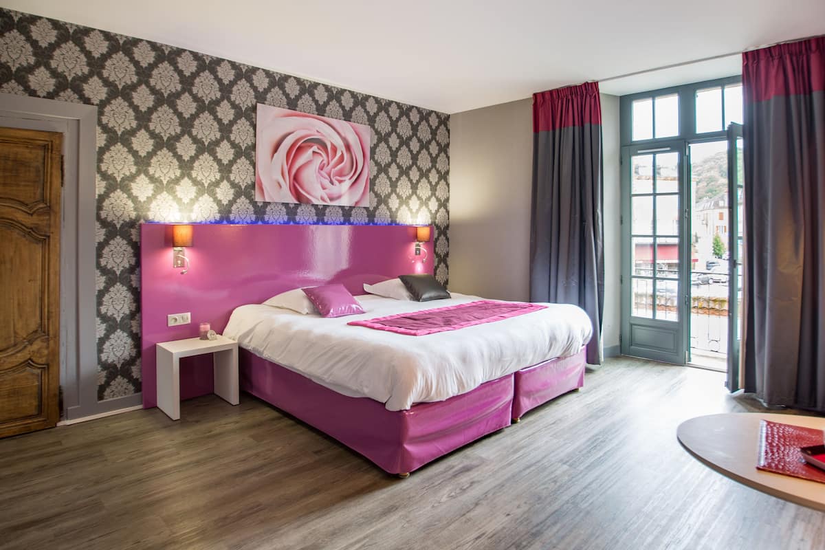 A modern bedroom with a pink bed, a nightstand, a wall-mounted lamp, and a large window with curtains.