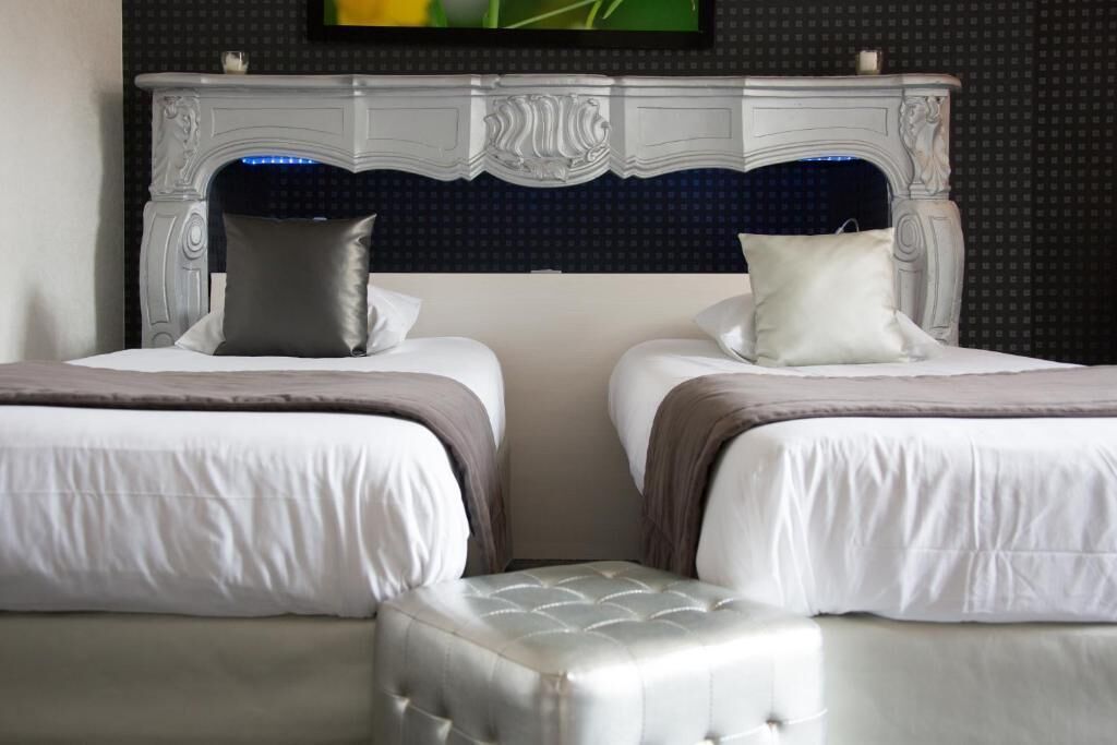 A hotel room with two beds, a decorative headboard, and a small ottoman.