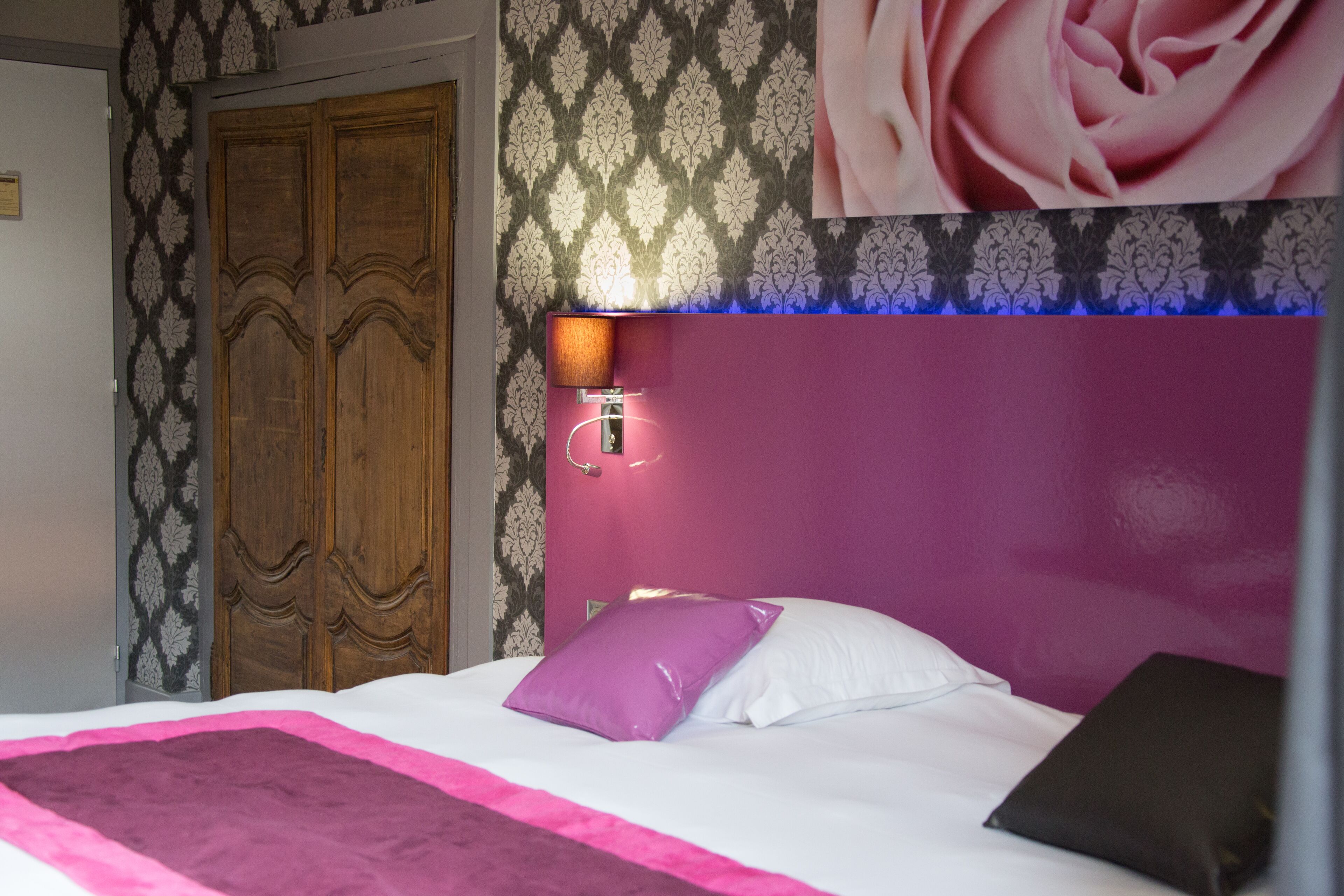 A bedroom with a bed, a wooden wardrobe, and a wall-mounted lamp.