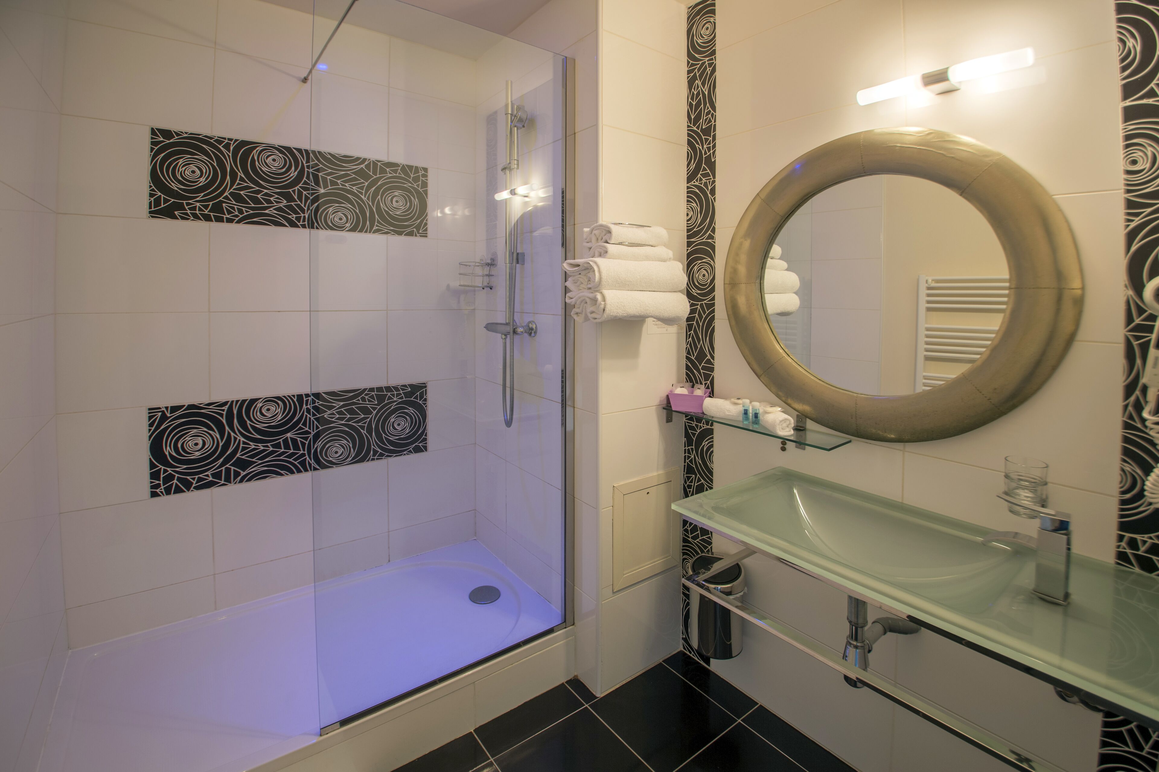 A modern bathroom with a glass-enclosed shower, a glass sink, and a large mirror.