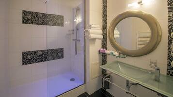 A modern bathroom with a glass-enclosed shower, a glass sink, and a large mirror.