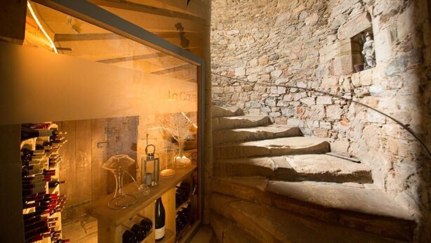 A wine cellar with stone walls and a spiral staircase. - Hôtel Le Turenne (Beaulieu-sur-Dordogne)