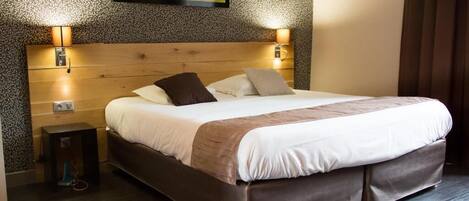 Een net opgemaakt bed met een houten hoofdbord, twee bedlampen en een klein nachtkastje met een lamp.