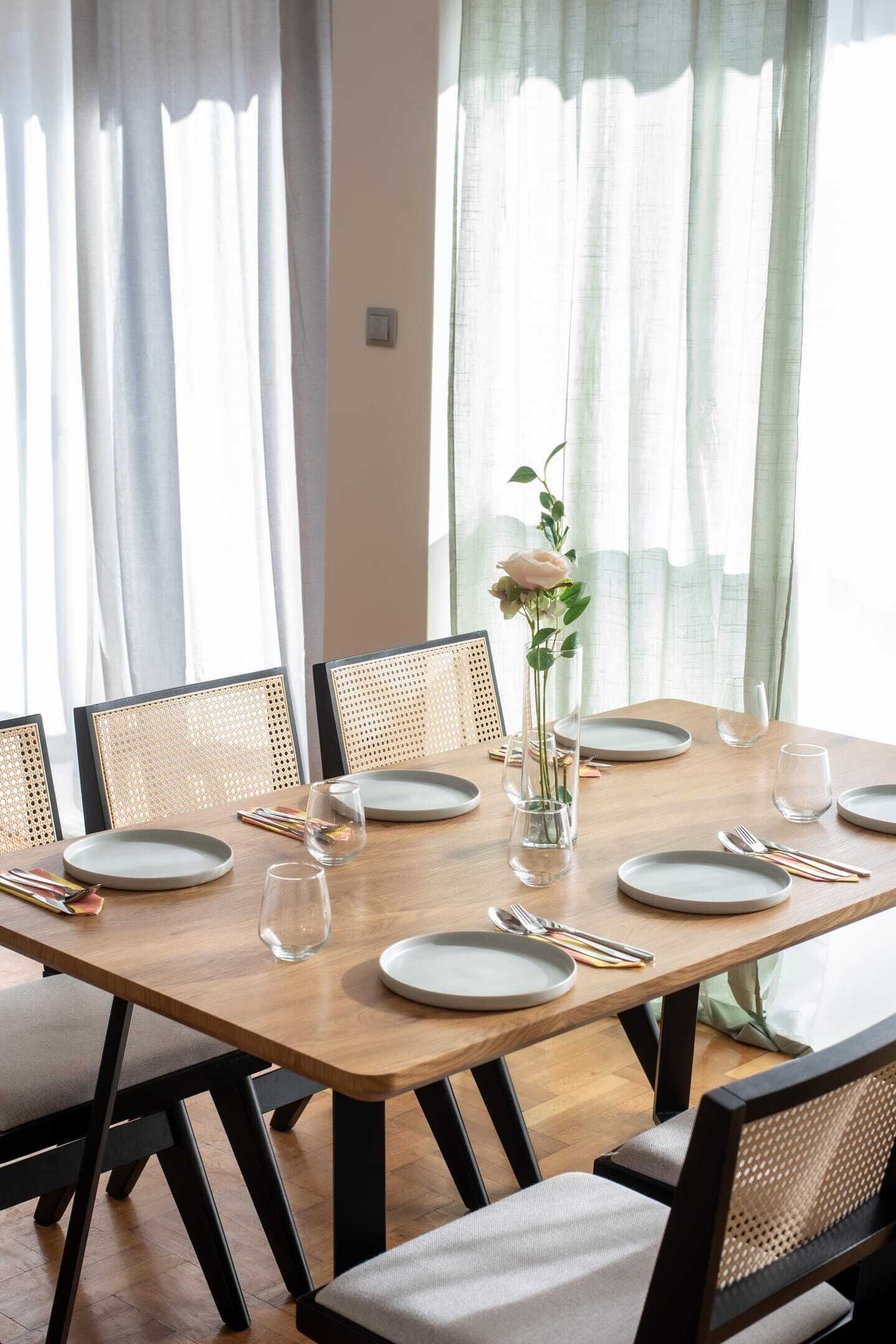 Une table à manger dressée pour six personnes, agrémentée d ’un vase de fleurs, de chaises en bois et d’une nappe de couleur claire.