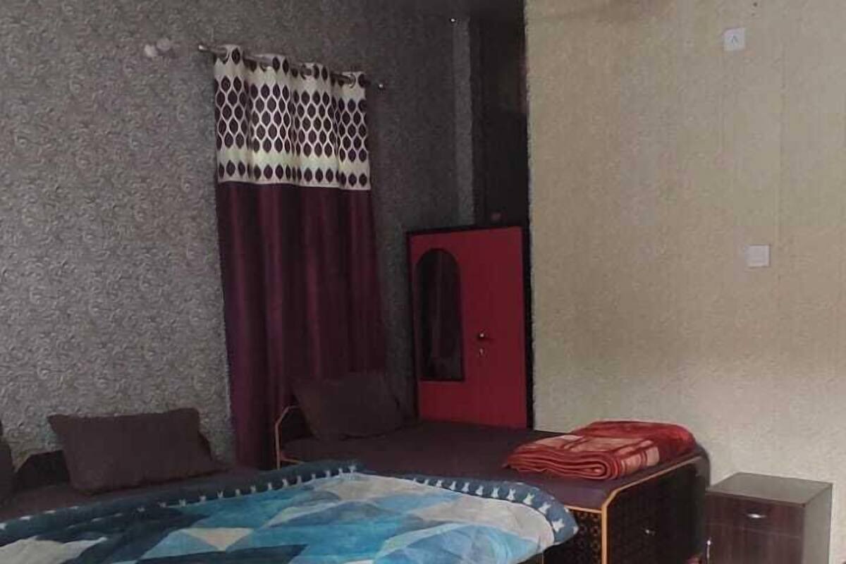 A room with a ceiling fan, patterned curtains, a bed with a quilt, a red cabinet, and a tiled floor.