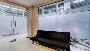 A room with a black leather sofa, a large window with a view of buildings, and a tiled floor. - Hotel O near Monas formerly Cideng Timur Residence (Jakarta)