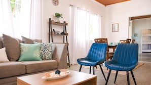 Ein Wohnzimmer mit einer Couch, zwei blauen Sesseln, einem Holztisch und einem Esstisch mit Stühlen.