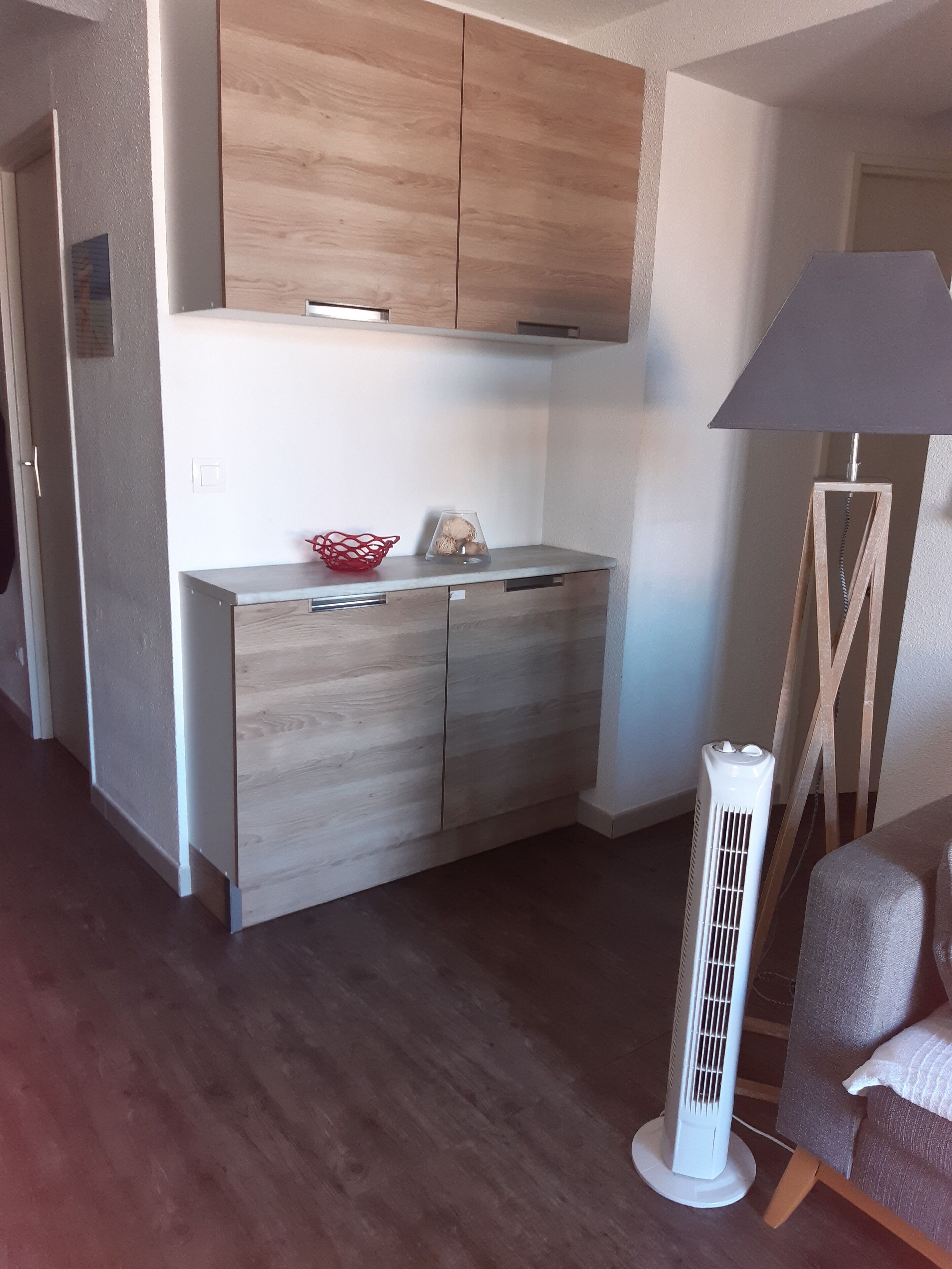 Una cocina moderna con armarios de madera, una encimera y una cesta roja. Hay un calentador blanco de pie y una lámpara cerca de la silla.