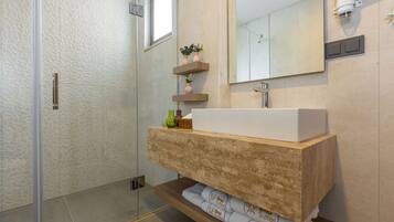 A modern bathroom with a glass shower enclosure, a wooden vanity with a white sink, and a mirror above it.