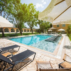 A swimming pool with lounge chairs and umbrellas, surrounded by trees and a building with arches. - Ema Houses (Antalya)