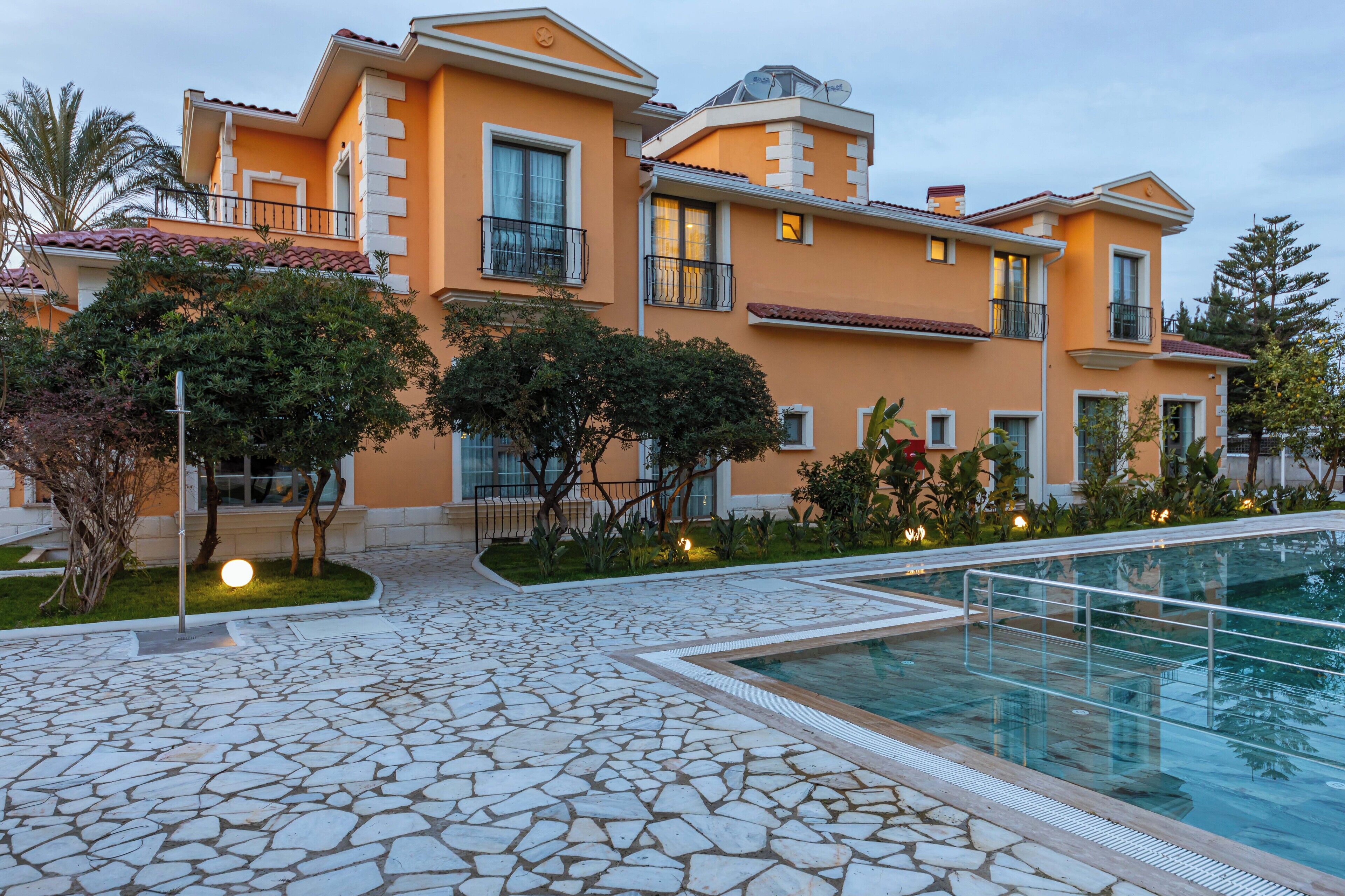 A multi-story hotel with a swimming pool, stone-tiled patio, and lush landscaping.