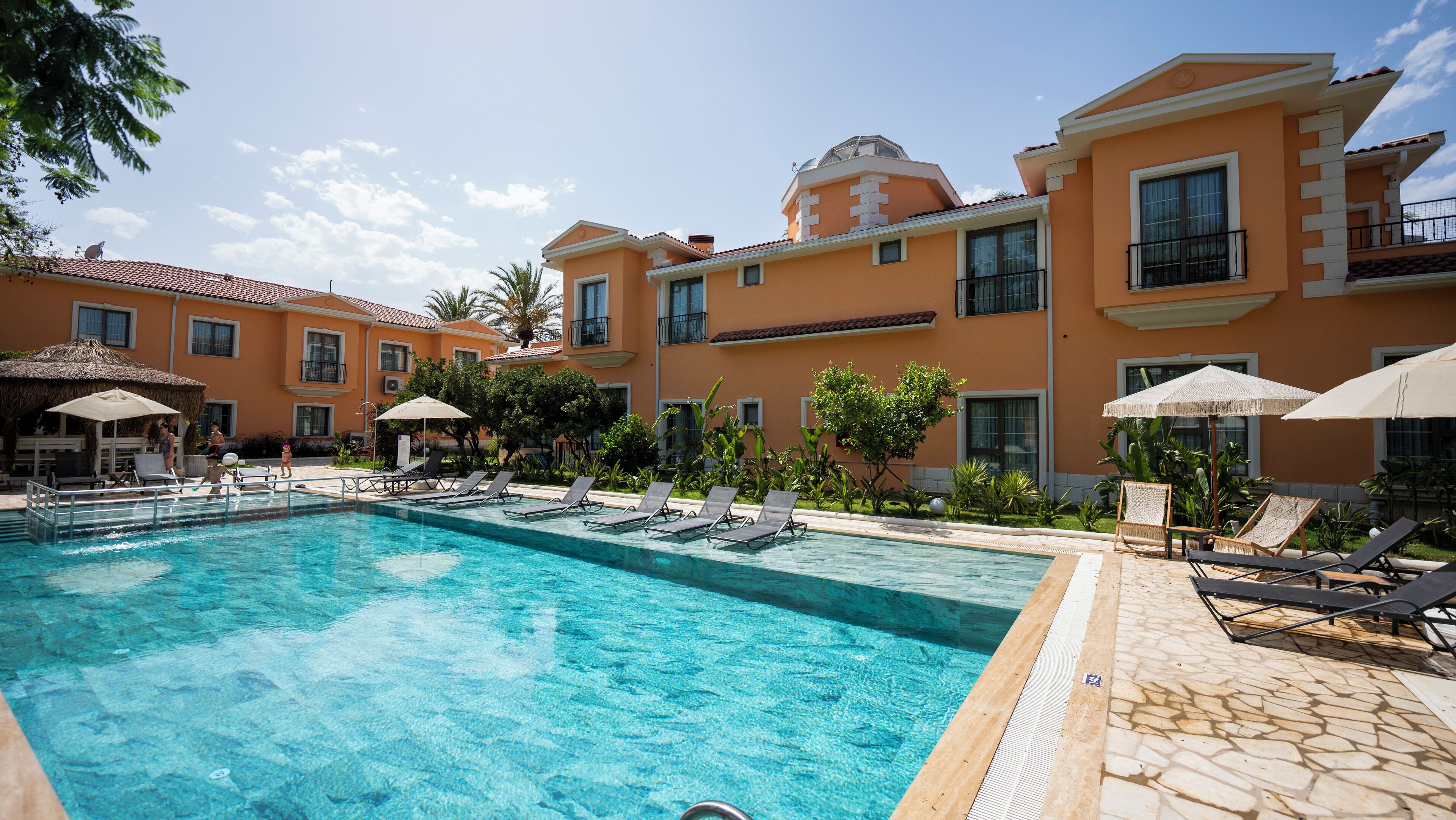 A swimming pool with lounge chairs and umbrellas, surrounded by a building with multiple windows and balconies.