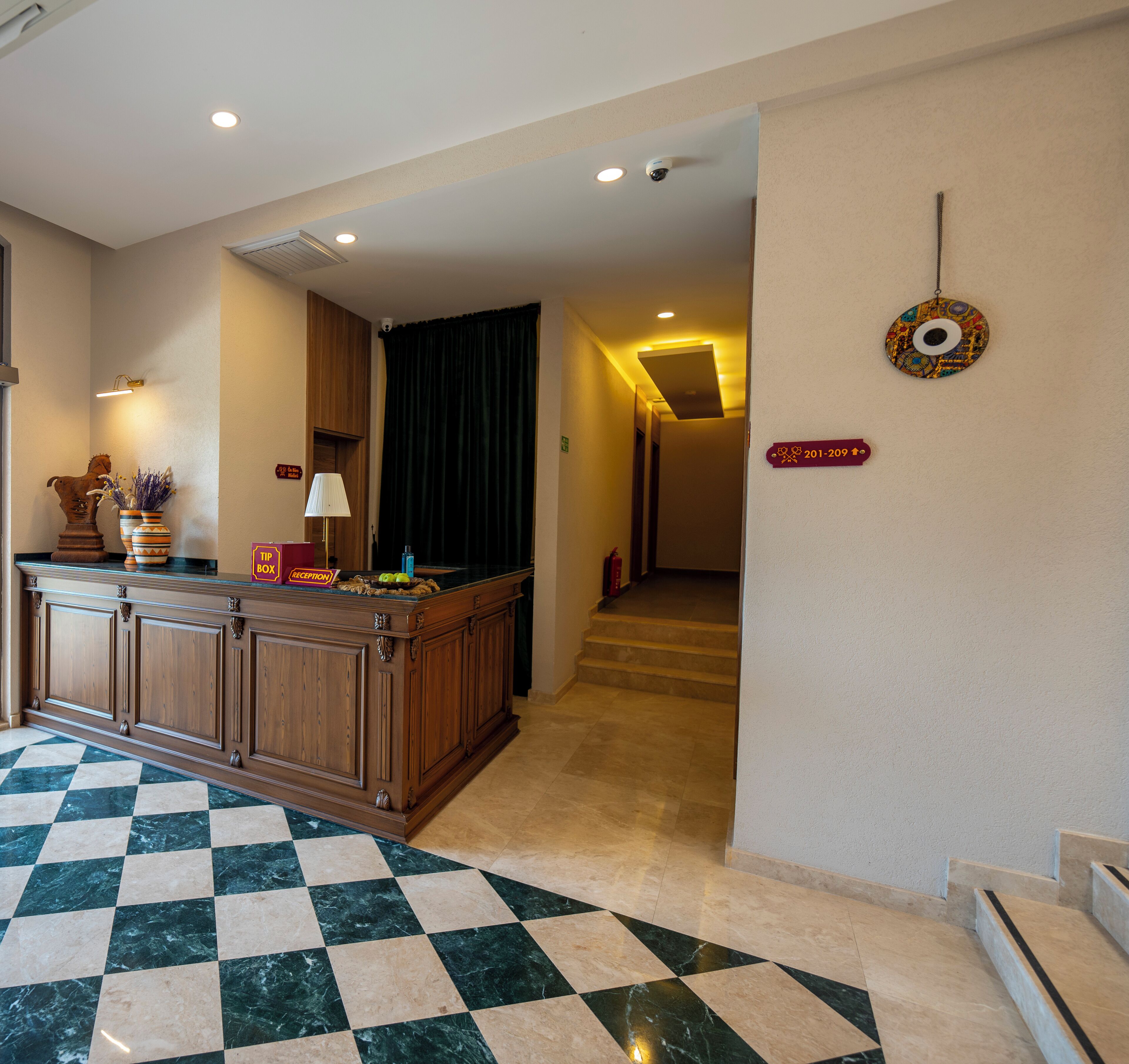 Un vestíbulo de hotel con mostrador de recepción, área de check-in, cartel de recepción, servicio de guardarropa y una escalera que conduce a los pisos superiores.