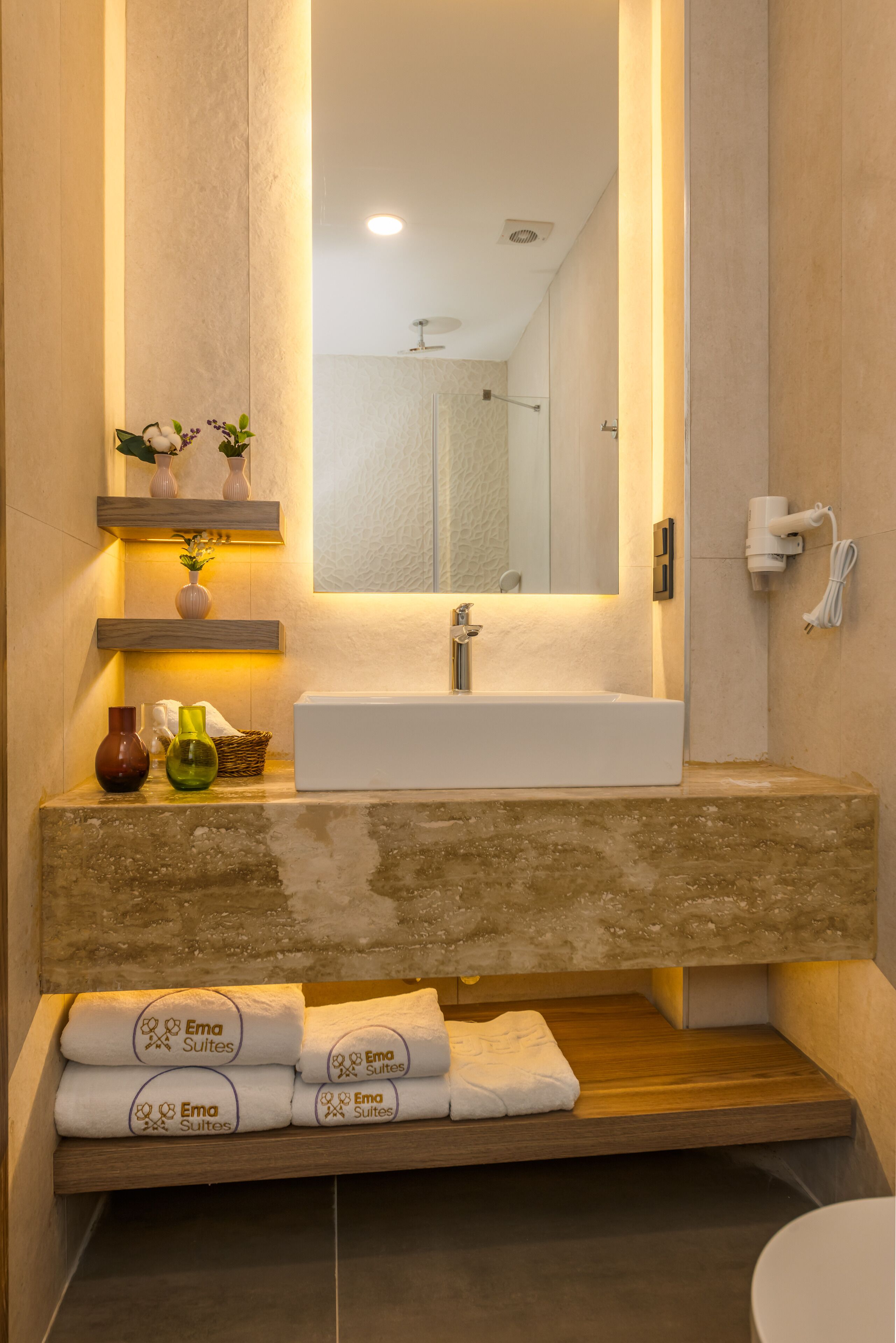 A modern bathroom with a large mirror, a white sink, and a shelf with decorative items.