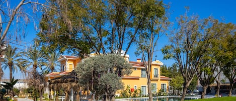 A yellow building with a pool, surrounded by trees and a pathway.