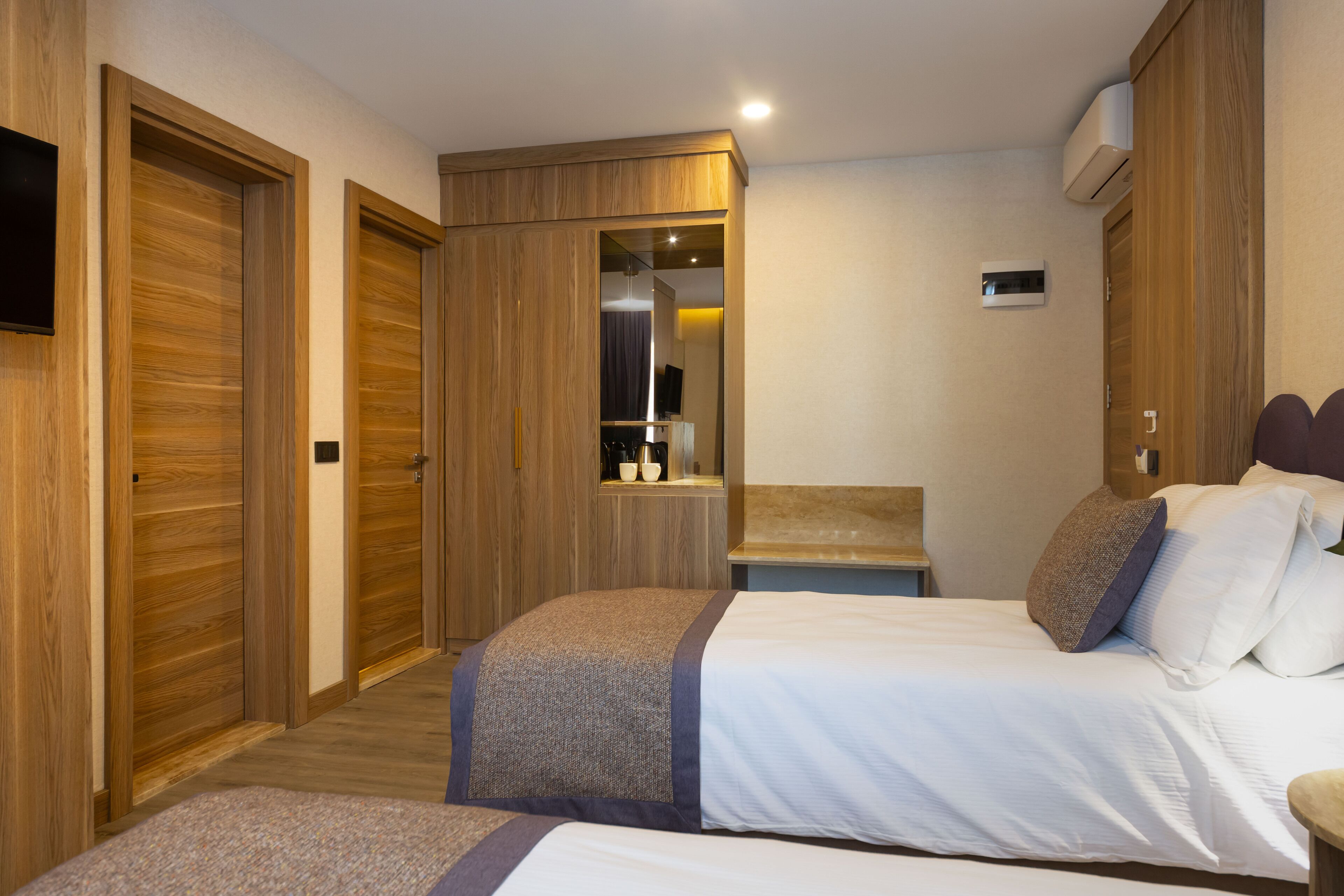 A hotel room with two beds, wooden wardrobes, a small table, and a mirror.