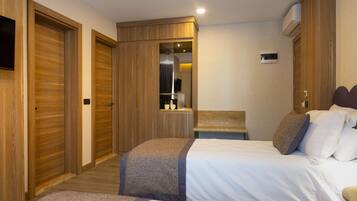 A hotel room with two beds, wooden wardrobes, a small table, and a mirror.
