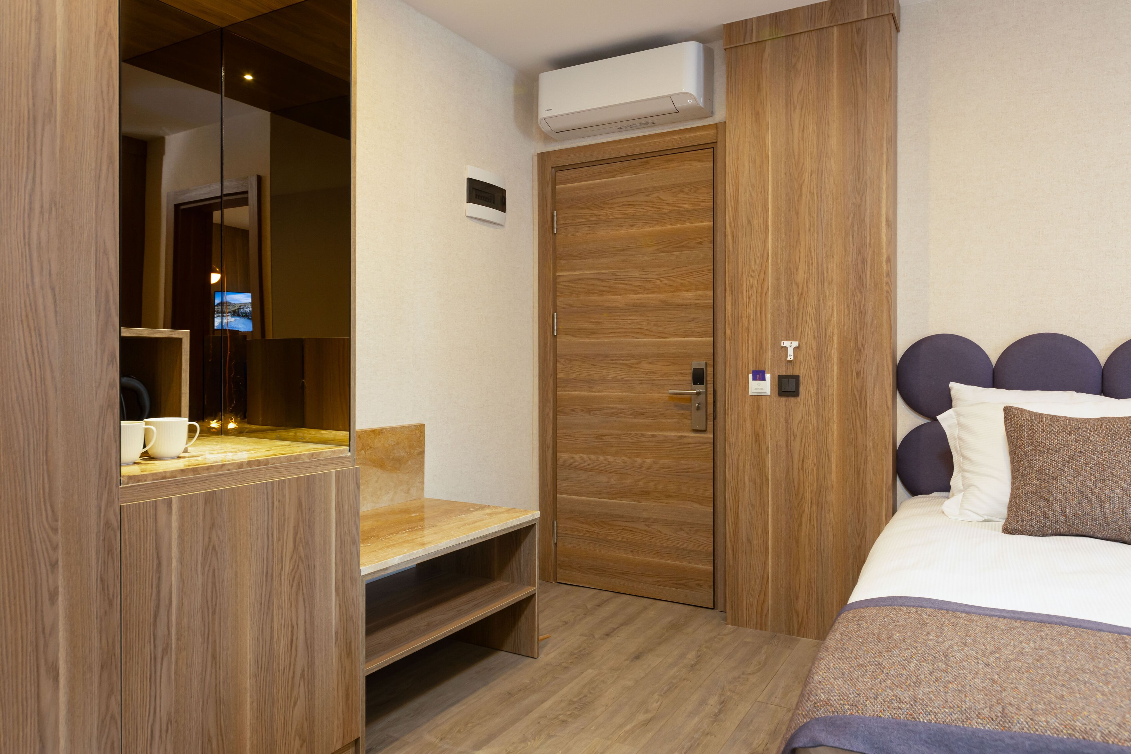 A bedroom with a wooden wardrobe, a bed with a headboard, and a small seating area with a table and chairs.