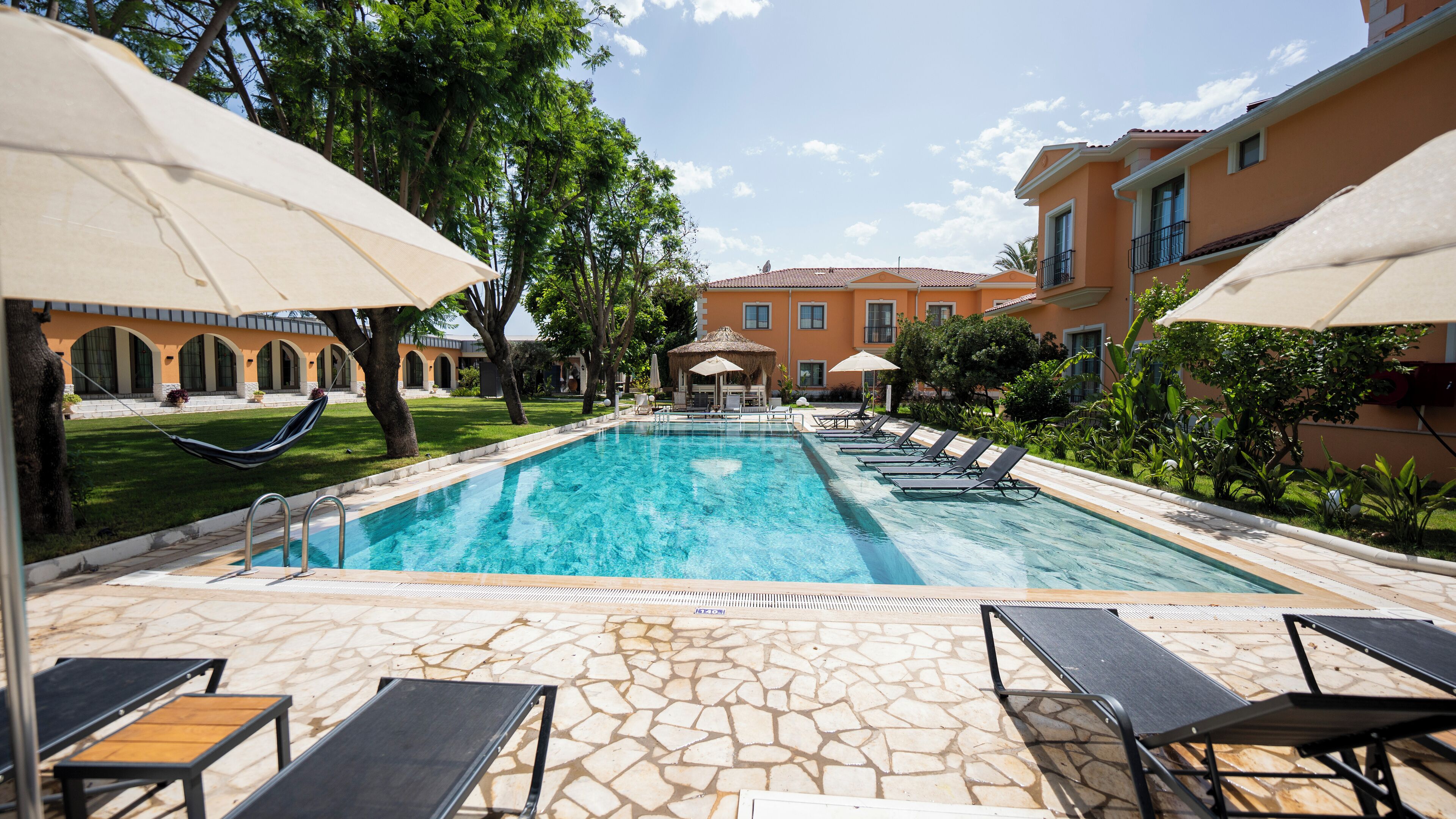 A swimming pool with lounge chairs and umbrellas, surrounded by a stone patio and greenery.