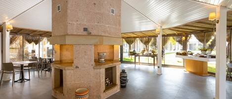 A spacious indoor area with a central stone fireplace, seating arrangements, and a view of the outdoors.