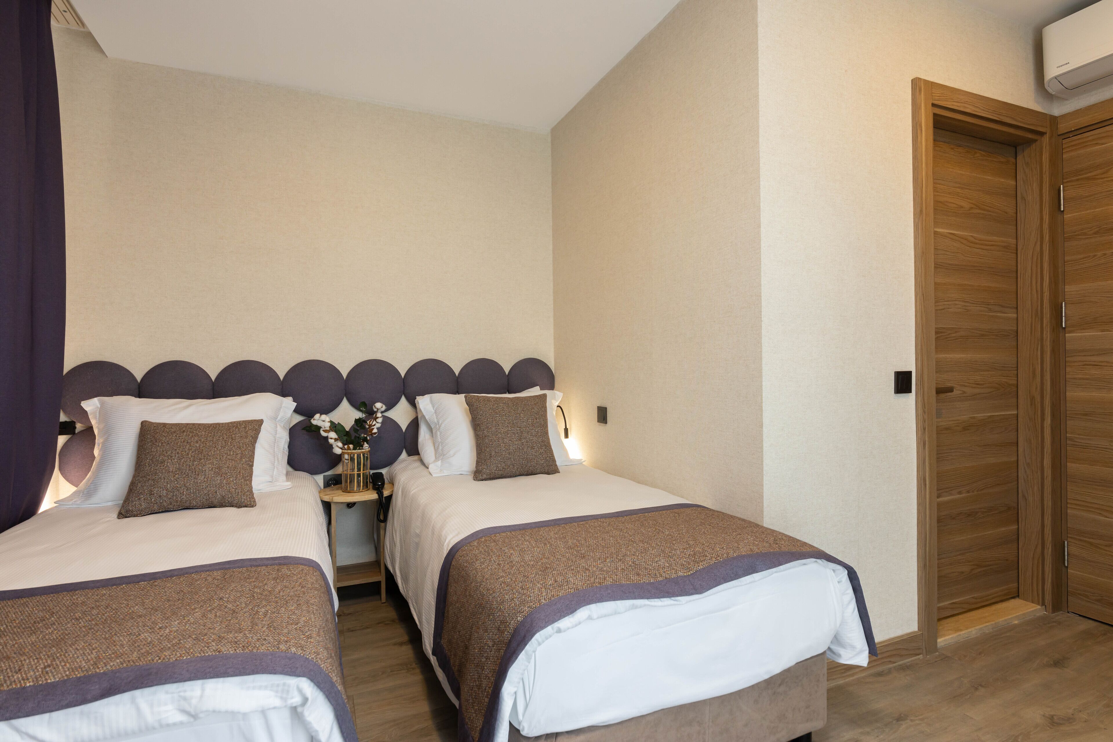 Un dormitorio con dos camas, un armario de madera y una mesita de noche con un jarrón de flores.