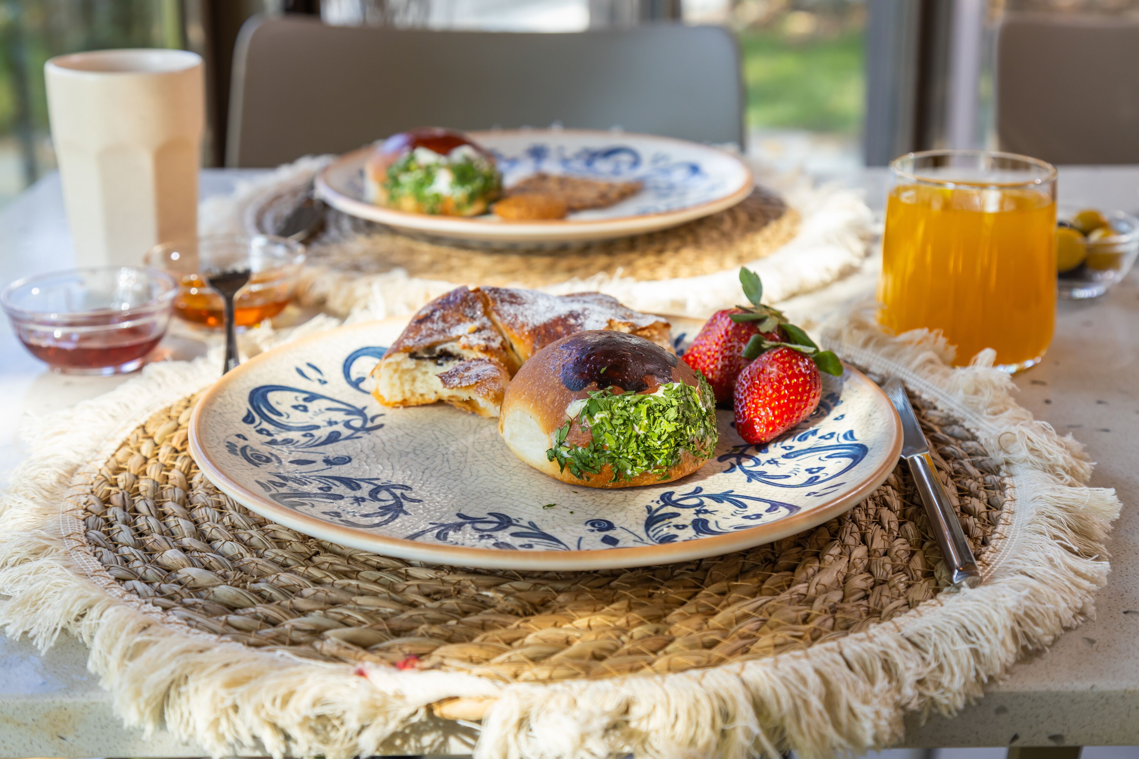 A table with a woven placemat, a plate with food, a glass of orange juice, and a cup.