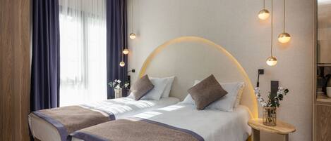 A modern hotel room with two beds, a wooden wardrobe, a round wall light, and a small table with a vase.