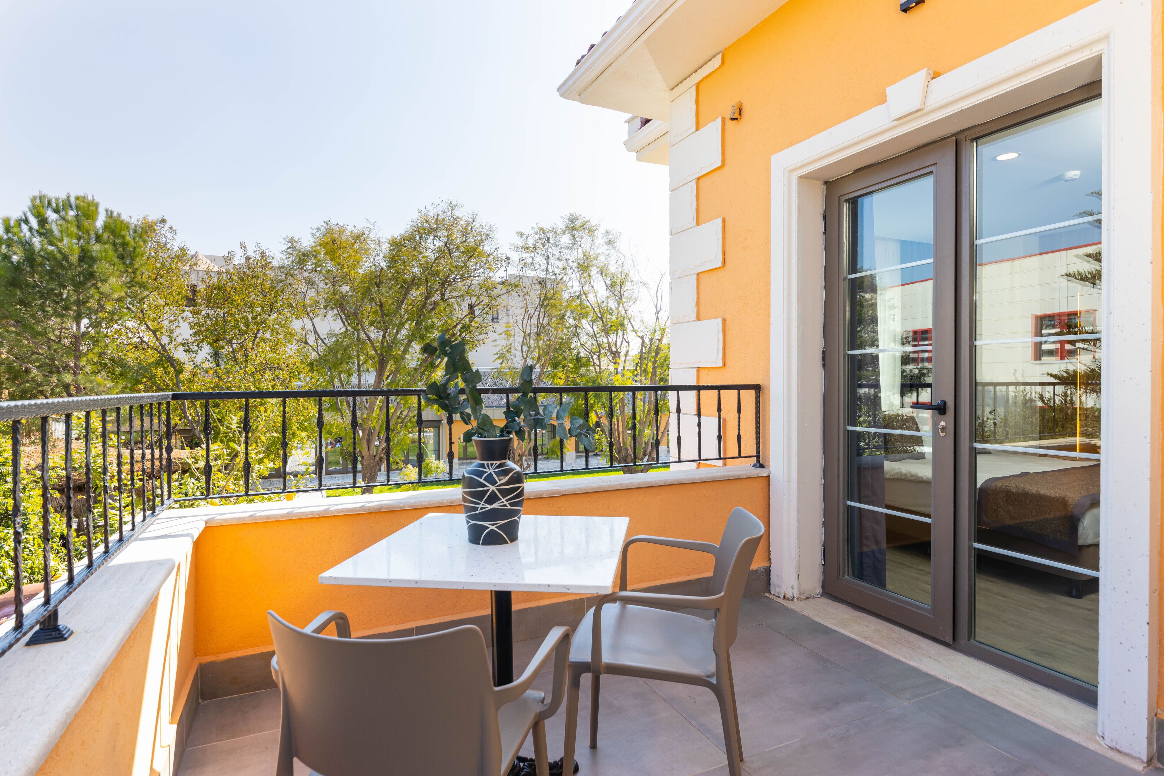 A balcony with a table and chairs, a potted plant, and a sliding glass door.