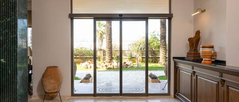 A spacious room with a large sliding glass door leading to a courtyard, a tiled floor, and a wooden cabinet with decorative items.