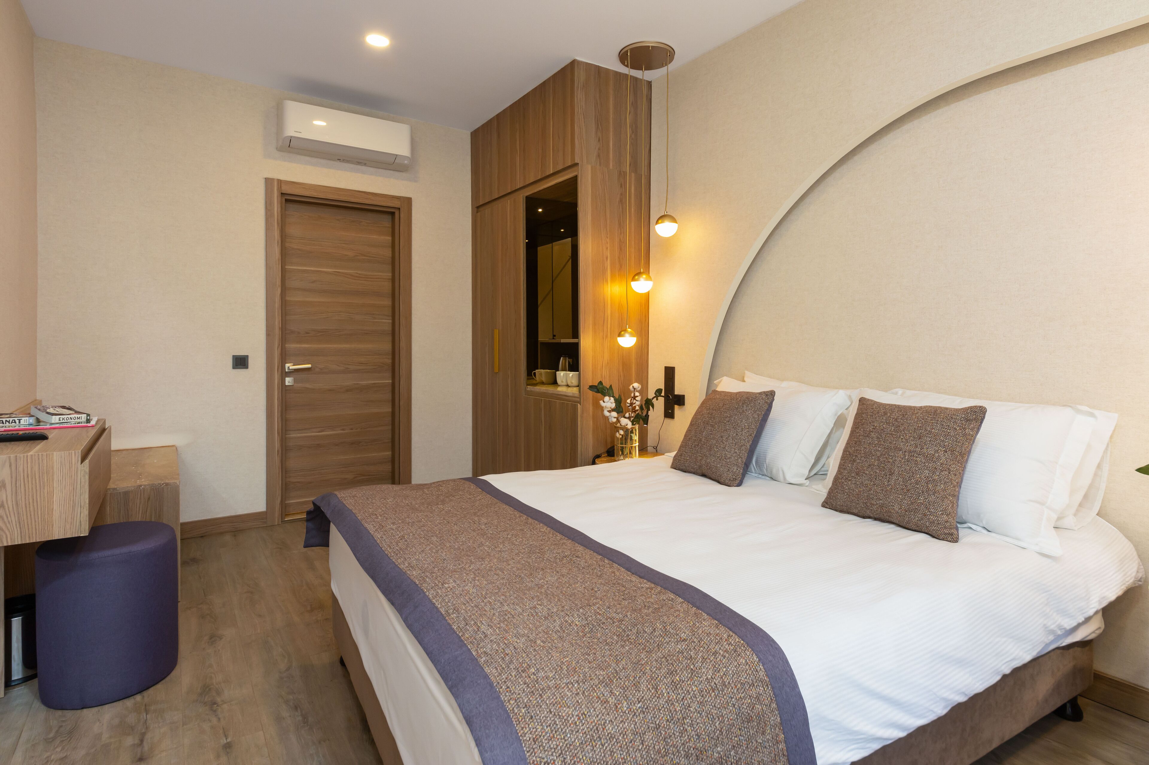 A modern bedroom with a wooden wardrobe, a desk with a chair, and a bedside table with a lamp.