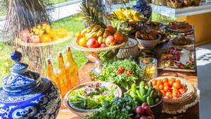 A table with various fruits, vegetables, and bread, set in a bright room with a view of greenery outside.