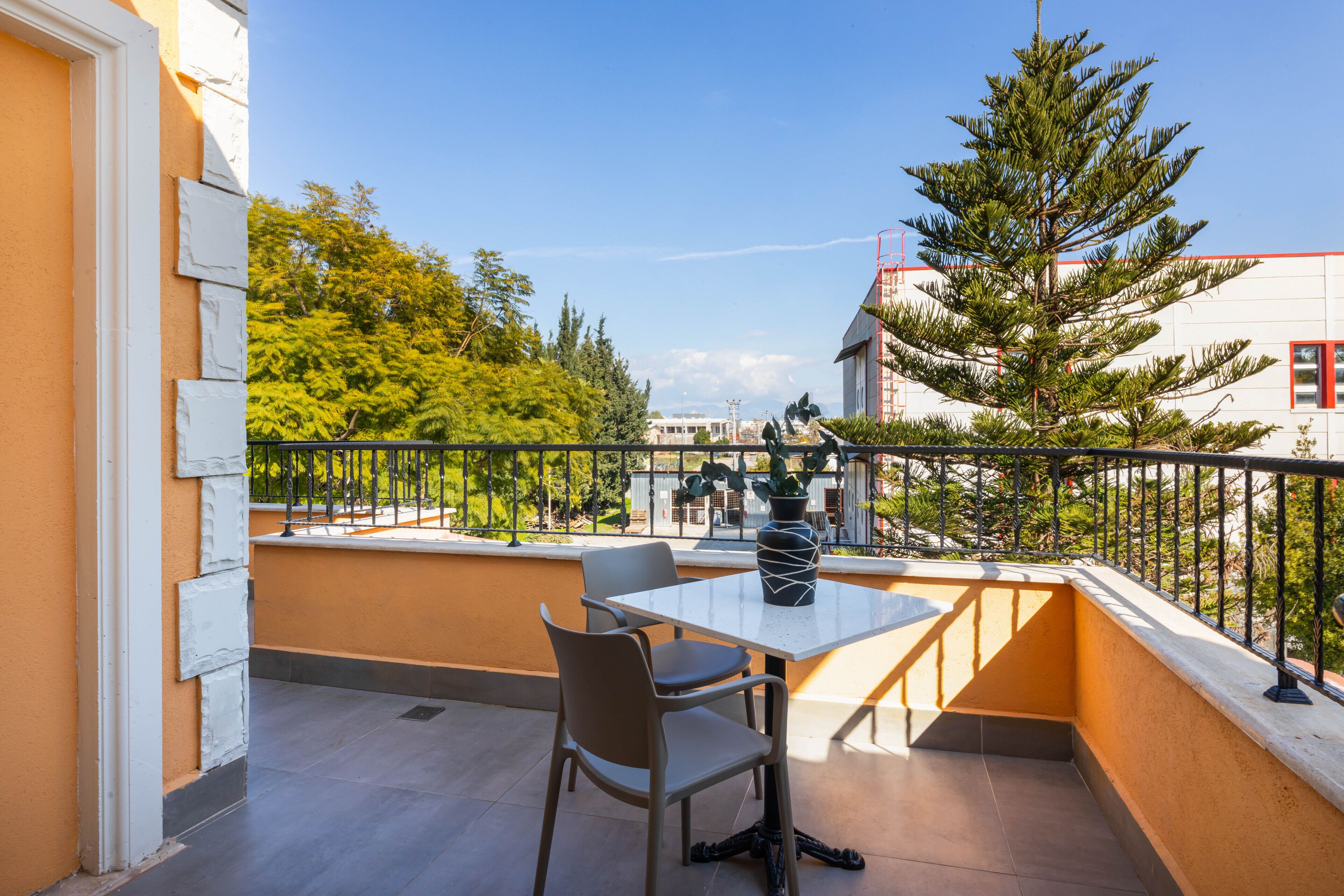 Ein Balkon mit Tisch und Stühlen, einem Blumentopf und Blick auf Bäume und Gebäude.